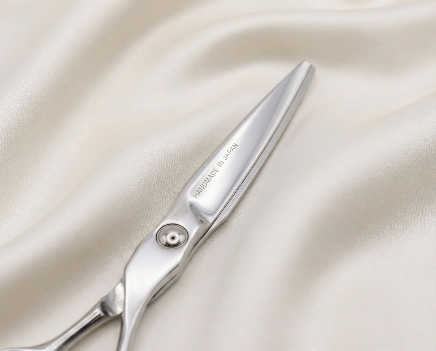 Friseurschere aus Edelstahl mit ergonomischem Design, handgefertigt in Japan auf hellem Stoff liegend