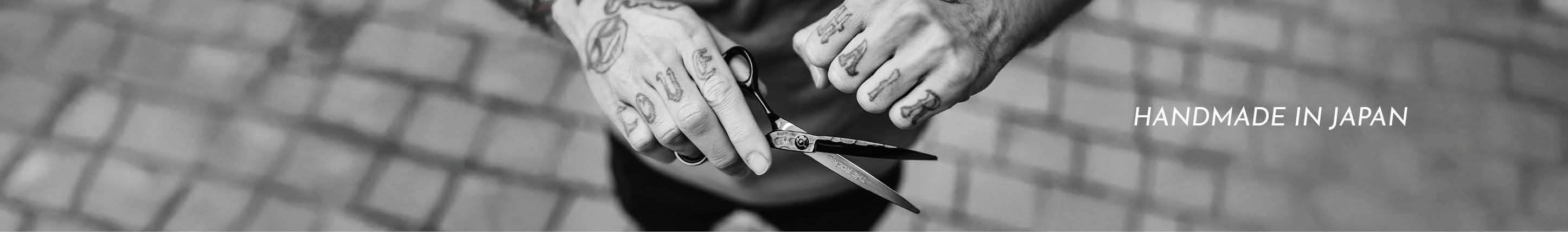 Schwarz-weiße Aufnahme von Händen, die eine Friseurschere in einem gepflasterten Außenbereich halten