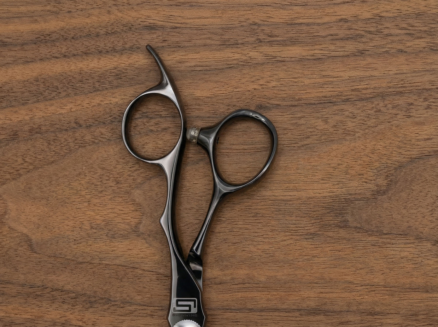 Shidosha Haarschneideschere aus schwarz beschichtetem Stahl mit ergonomisch geformtem Griff auf Holzuntergrund