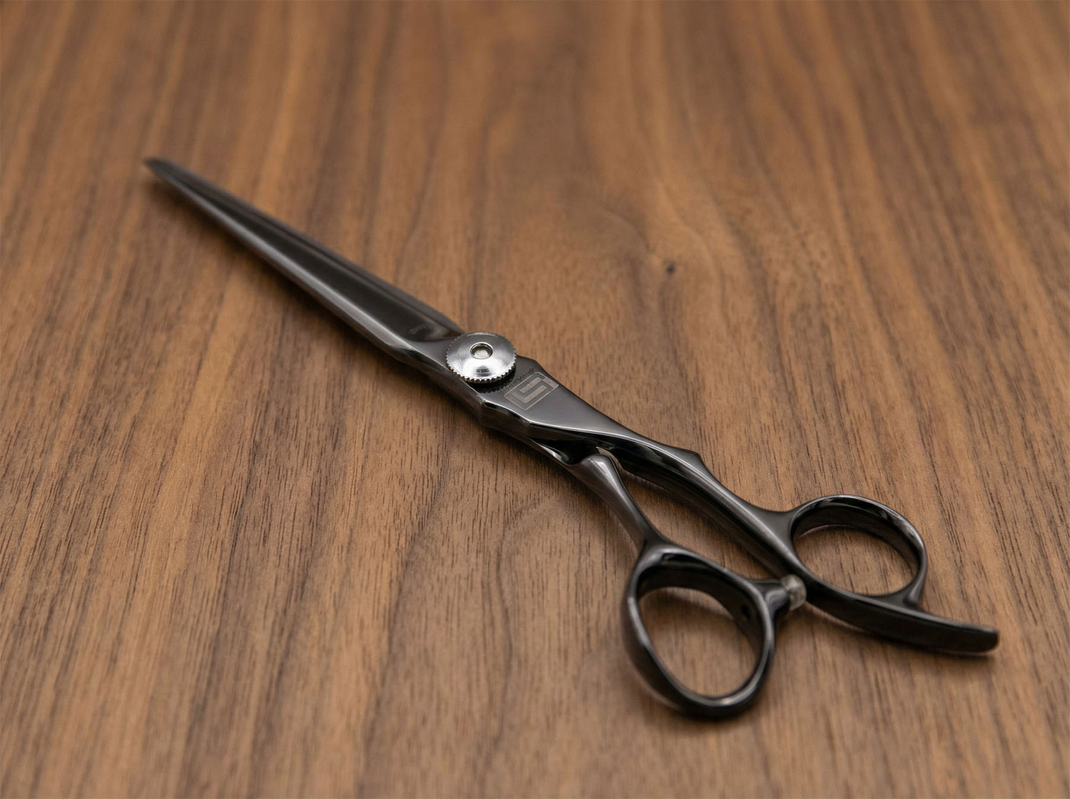 Shidosha Haarschneideschere aus schwarz beschichtetem Stahl mit ergonomisch geformtem Griff auf Holzuntergrund