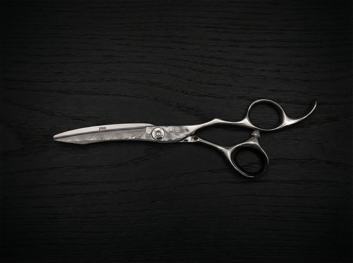Diavolo Haarschneideschere aus poliertem Stahl mit gebogener Klinge und feiner Verzierung auf dunklem Holzuntergrund