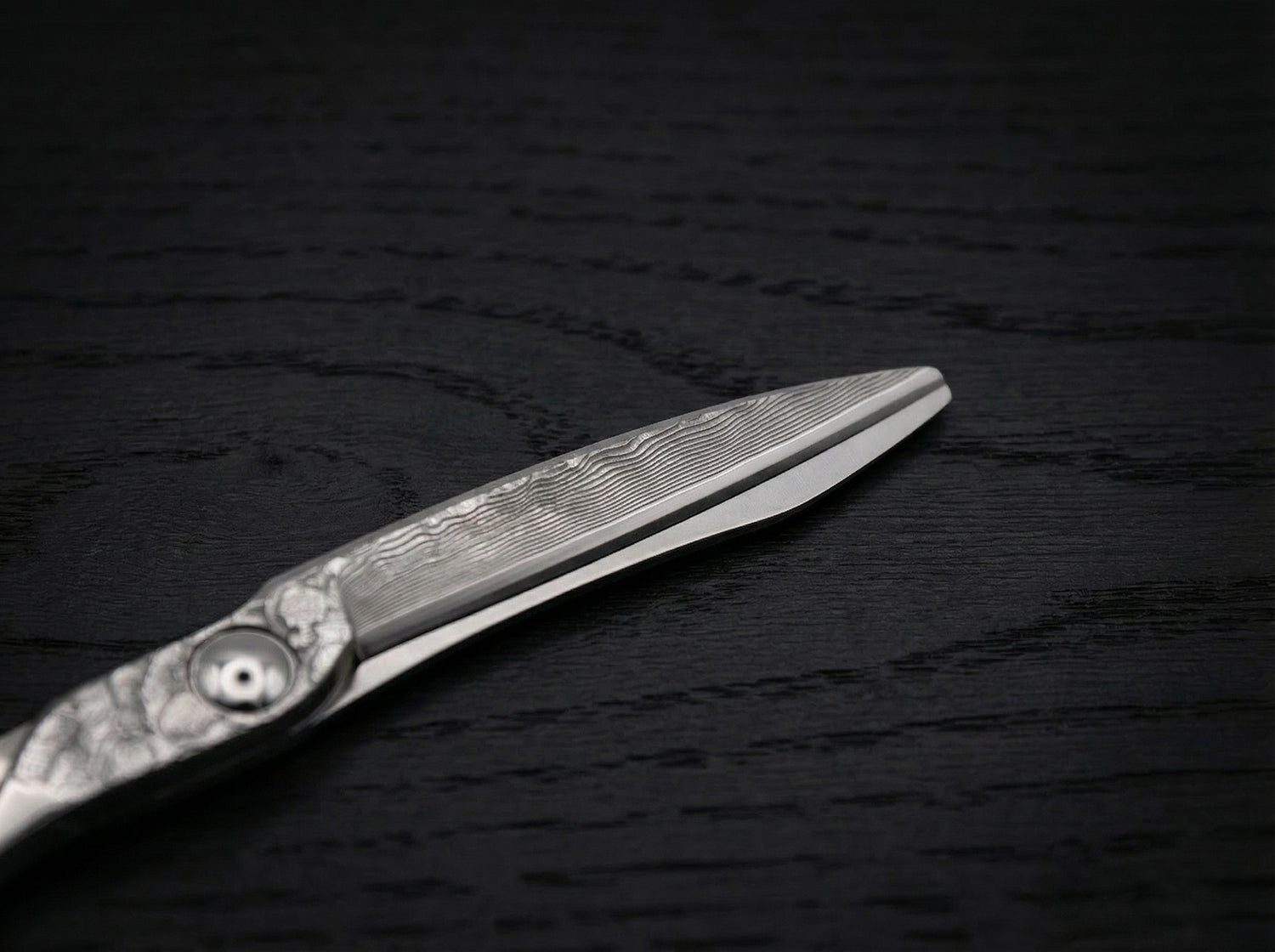 Diavolo Friseurschere aus Damaststahl mit filigraner Klingenstruktur und gerader Schneide auf dunklem Holzuntergrund