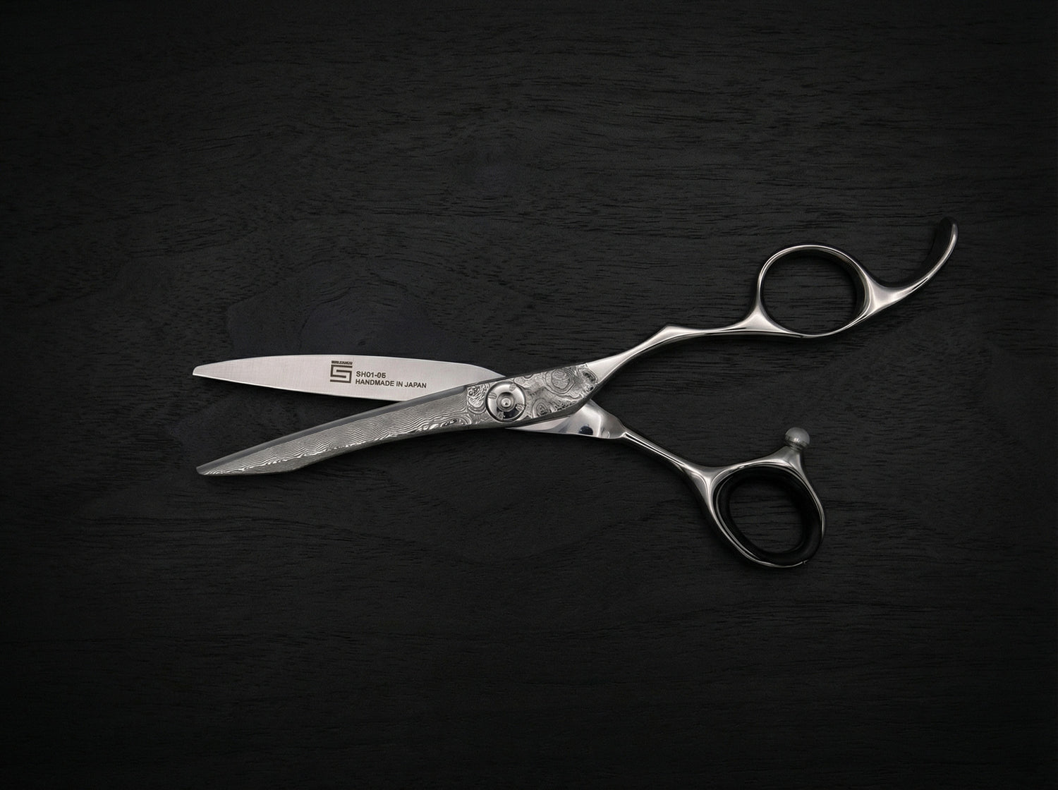 Leader Haarschneideschere aus poliertem Stahl mit ergonomisch geformtem Griff und feiner Klingenverzierung auf dunklem Untergrund