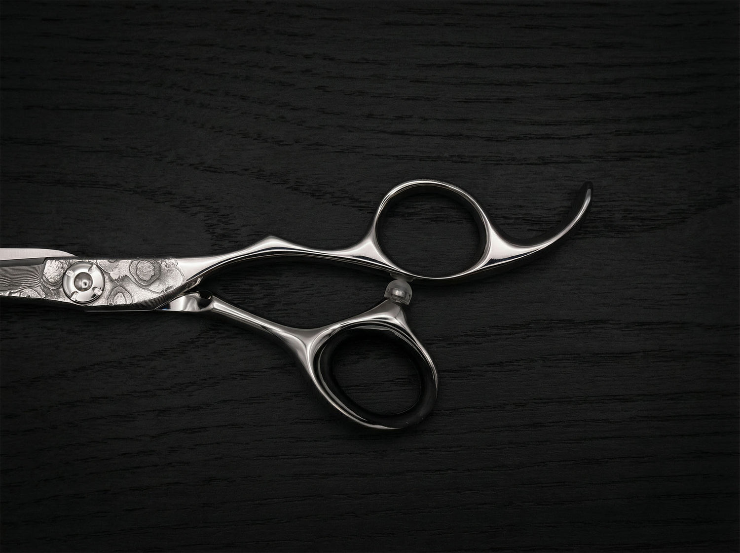 Diavolo Haarschneideschere aus poliertem Stahl mit geschwungenem Griff und filigraner Klingenverzierung auf dunklem Holzuntergrund