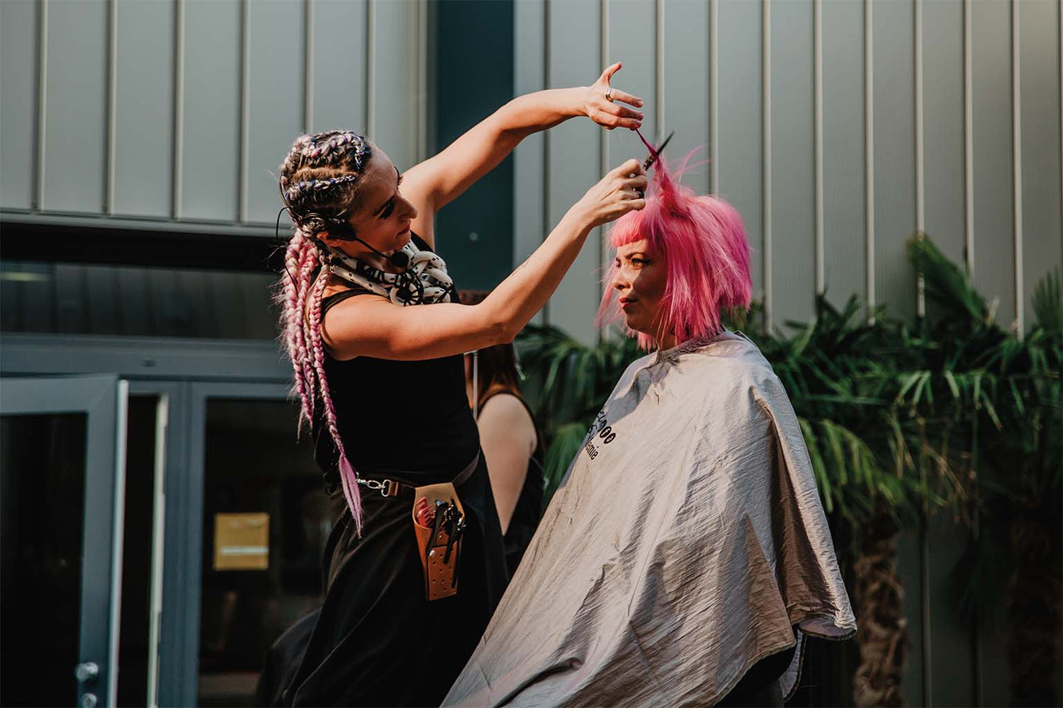Friseur schneidet pink gefärbtes Haar mit Haarschneideschere in Freiluftumgebung bei Tageslicht