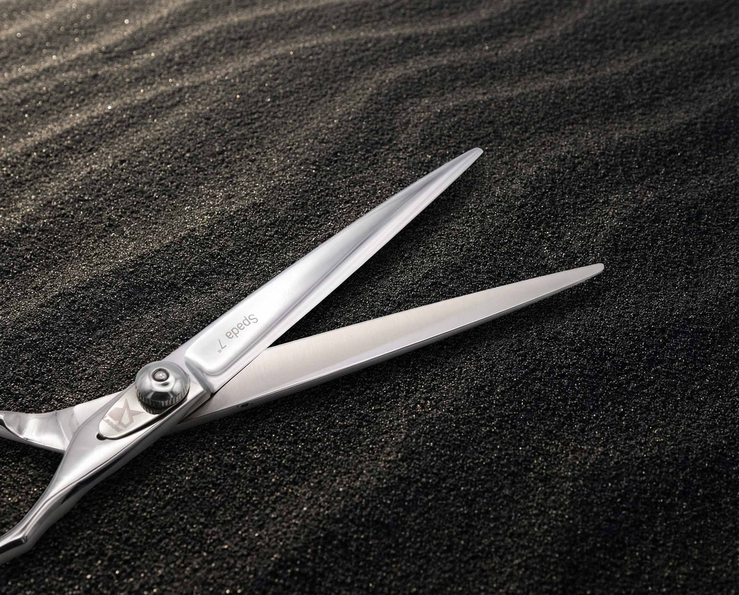 Elegante, polierte Friseurschere mit spitzen Klingen auf feinkörnigem, schwarzem Sand liegend